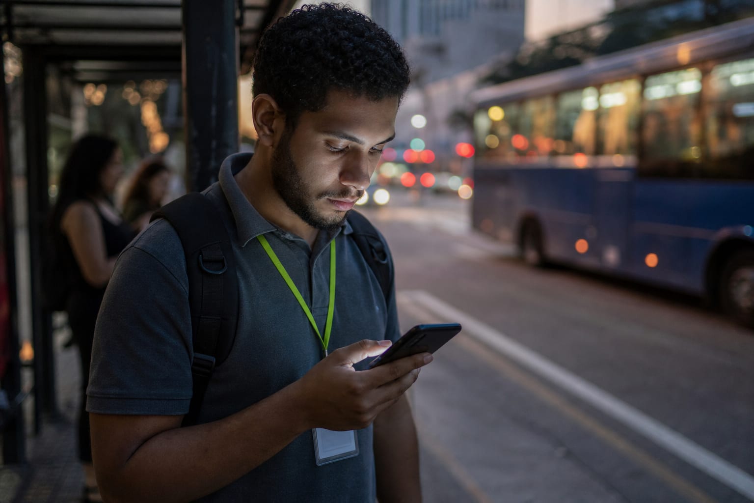 Trabalhador de uniforme em um ponto de ônibus olhando o celular no fim da tarde